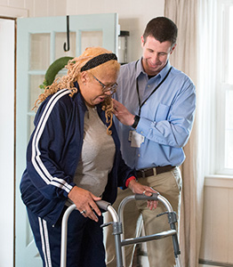 male caregiver helping senior woman walking with an assistive walker